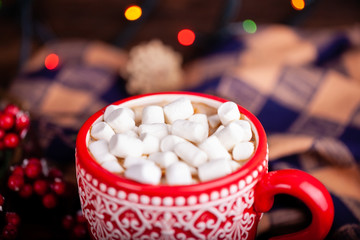 Close-up of red cup with ornament with hot cocoa drink and cute mini marshmallows on lights bokeh decorations background. Christmas and New Year holidays concept.