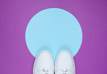 White sneakers on purple background with blue pastel circle for copy space. Youth hipster concept. Top view
