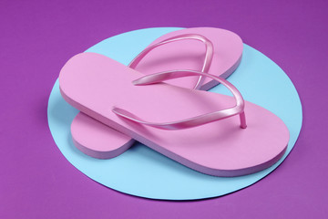 Pink flip flops on purple background with blue pastel circle. Minimalistic vacation on the beach concept. Summer time