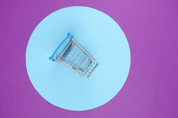 Shopping cart on purple background with blue pastel circle. Minimalistic shopping concept,...