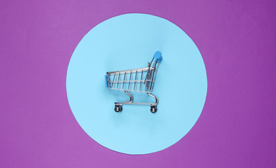 Shopping cart on purple background with blue pastel circle. Minimalistic shopping concept,...
