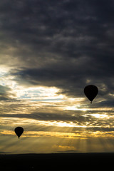 Masai Mara, Kenya. Pair of hot air balloons carrying tourists in flight as the sun breaks through heavy clouds.