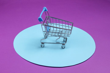 Shopping cart on purple background with blue pastel circle. Minimalistic shopping concept,...