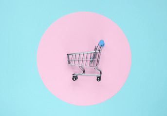 Shopping cart on blue background with pink pastel circle. Minimalistic shopping concept,...
