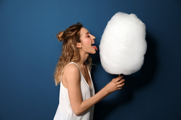 Portrait of pretty young woman with cotton candy on blue background