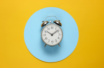 Retro alarm clock on yellow background with blue pastel circle. Top view