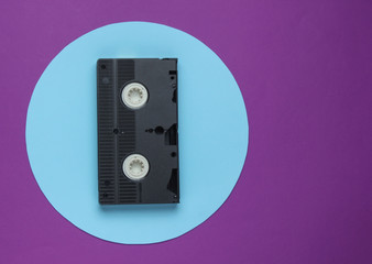 Fototapeta premium Video cassette on purple background with blue pastel circle. Minimalistic retro concept. 80s. Top view