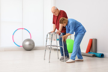 Caretaker helping elderly man with walking frame indoors