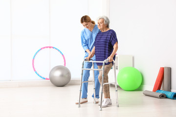 Caretaker helping elderly woman with walking frame indoors