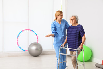 Caretaker helping elderly woman with walking frame indoors