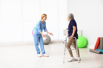 Caretaker helping elderly woman with walking frame indoors