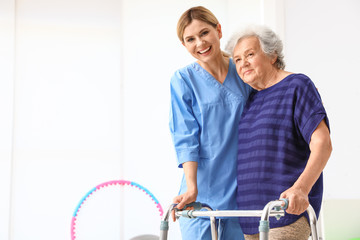 Caretaker helping elderly woman with walking frame indoors