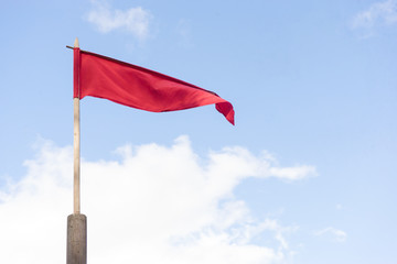 narrow red swinging flag on wooden flagpole against sky
