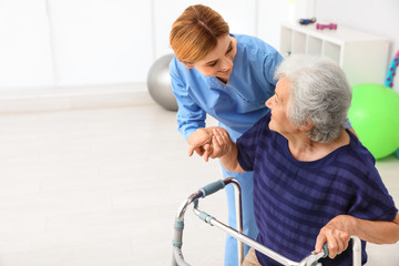 Caretaker helping elderly woman with walking frame indoors