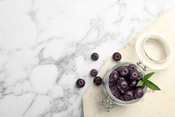 Jar of fresh acai berries with board on marble table, flat lay. Space for text