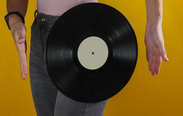 Woman in jeans with vinyl record on yellow background. Crop photo