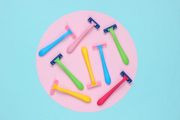 Many colored plastic razors on blue background with pink pastel circle. Minimalistic beauty still life