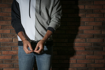 Male criminal in handcuffs near brick wall, closeup. Space for text