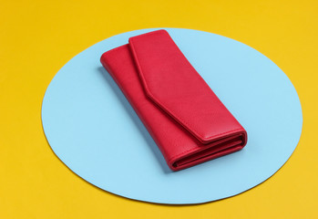 Stylish women's red leather wallet on yellow background with blue pastel circle. Creative minimalistic fashion still life