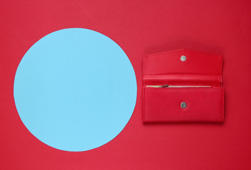 Stylish women's red leather wallet on red background with blue pastel circle for copy space. Creative minimalistic fashion still life. Top view