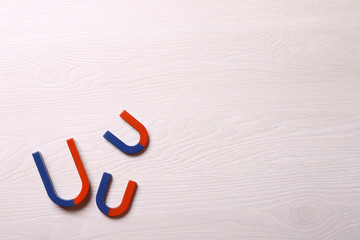 Red and blue horseshoe magnets on light wooden background, flat lay. Space for text