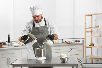 Male pastry chef preparing dough in mixer at kitchen table