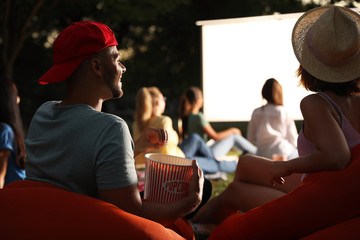 Young couple with popcorn watching movie in open air cinema. Space for text - obrazy, fototapety, plakaty