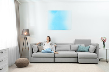 Happy young woman sitting under air conditioner at home