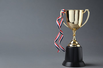 Golden trophy cup with ribbon on grey background. Space for text