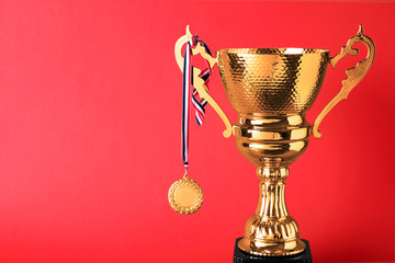 Golden trophy cup and medal on red background. Space for text
