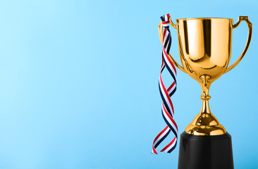 Golden trophy cup with ribbon on blue background. Space for text