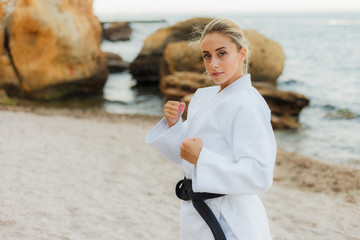 Attractive female martial artist in a white kimono with a black belt stands in fighting stance on...