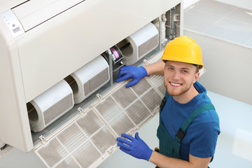 Professional technician maintaining modern air conditioner indoors