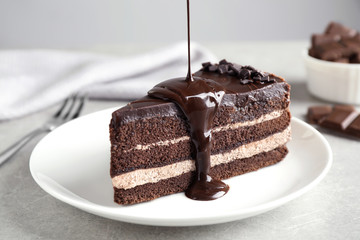 Pouring chocolate sauce onto delicious fresh cake on light table, closeup