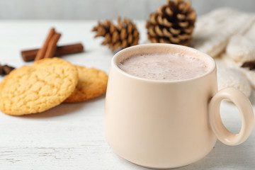 Delicious hot cocoa drink in cup and cookies on white wooden table, closeup