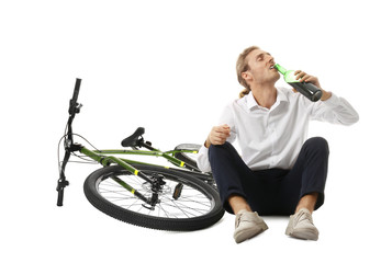 Fototapeta na wymiar Depressed young man with bottle of wine near bicycle on white background
