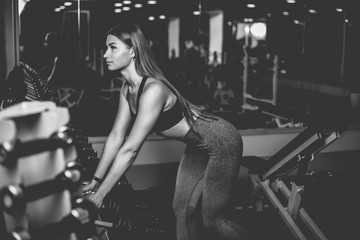 Young fit woman in sportswear takes heavy dumbbells from a rack in the gym. Healthy lifestyle concept.