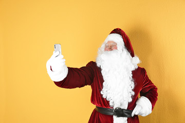 Fototapeta na wymiar Authentic Santa Claus taking selfie on yellow background