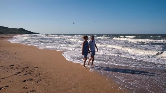 People, a man and a woman walk along the sandy beach and admire the sea waves on a Sunny summer day.