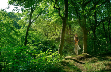 A woman practices yoga alone in the forest. Back view Spiritual Travel Relaxation Lifestyle Concept Harmony with nature. Modern for lifestyle design Body relaxation Asana yoga pose.