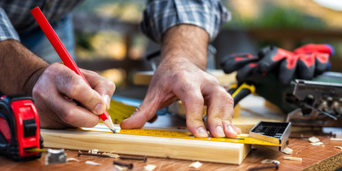 Adult carpenter craftsman with a pencil and the carpenter's square trace the cutting line on a...
