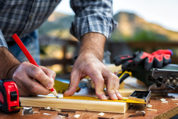 Adult carpenter craftsman with a pencil and the carpenter's square trace the cutting line on a wooden table. Construction industry, housework do it yourself. Stock photography.