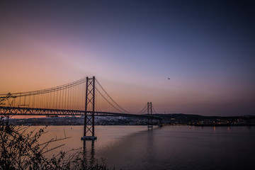 The 25 de April Bridge in Sunset Lights. Amazing view on Tagus River and one of the most famous and popular tourist sights in Lisbon. Portugal's beautiful landmark