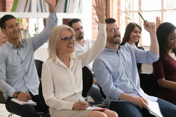 Motivated diverse employees raise hand participating in training