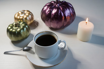 On a light table, a cup of coffee and ceramic pumpkins. Halloween