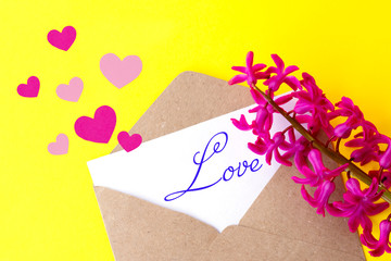 Love envelope and letter with written word love and pink hyacinth flowers with pink hearts on bright yellow bacground.