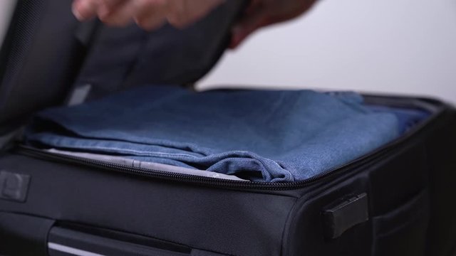 Close-up demonstration video of a man finishing to pack his suitcase and closing double zipper on the travel bag. Travel and luggage concept. Selective focus shot