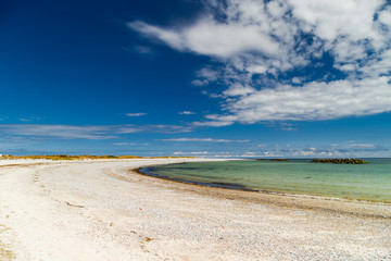 Fototapeta premium Küstenstrand mit grünem Wasser vor Horizont mit blauem Himmel und Wolken