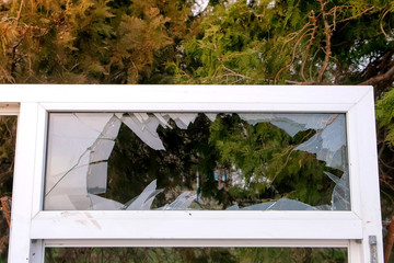 Part of white window frame with broken glass on the background of trees in the city Park. Dismantling and destruction of old buildings.