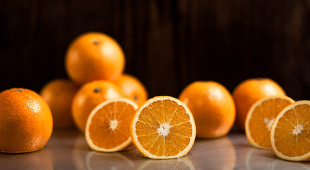 A group of delicious fresh oranges on a gray table with a sliced orange in the middle on dark background.